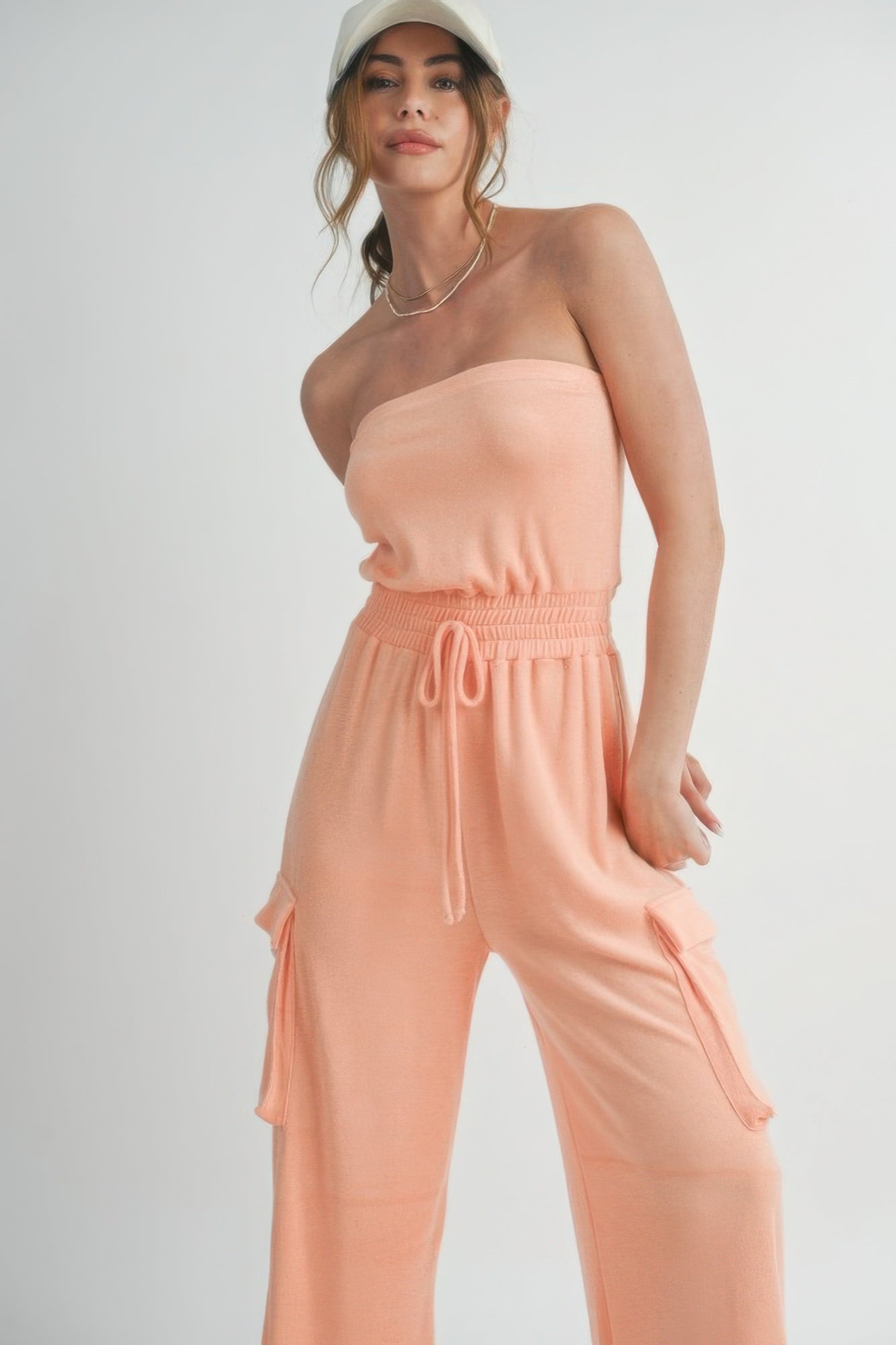 Close-up of smocked waist and cargo pocket on peach jumpsuit.