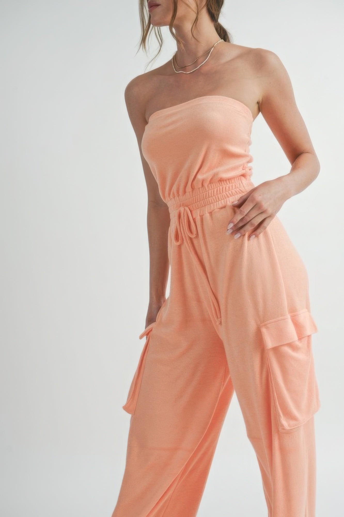 Close-up of smocked waist and cargo pocket on peach jumpsuit.