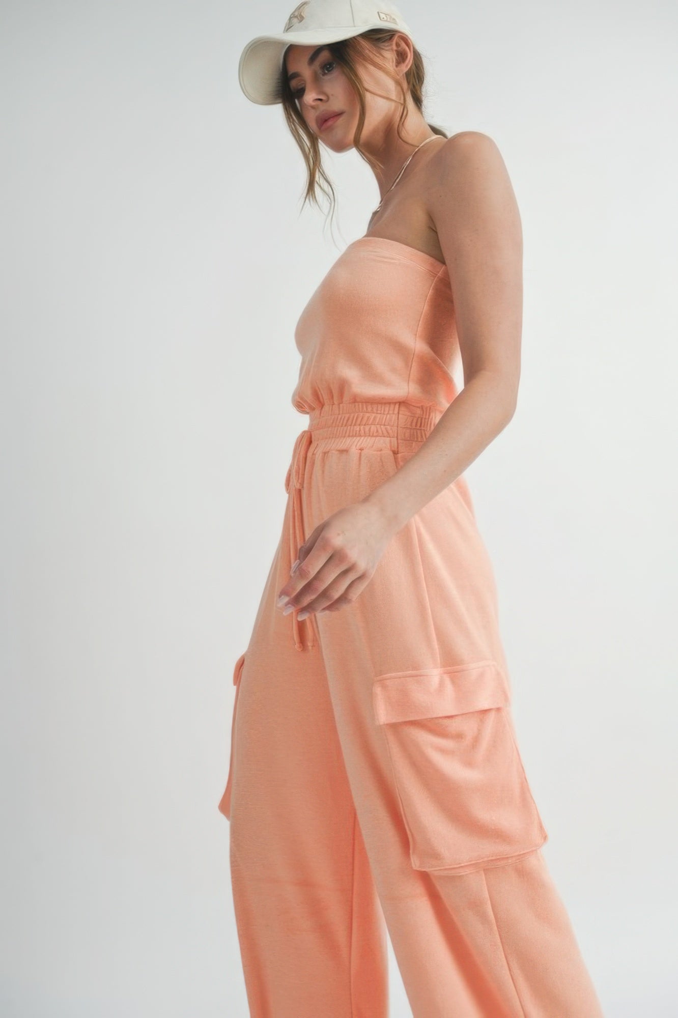 Close-up of smocked waist and cargo pocket on peach jumpsuit.
