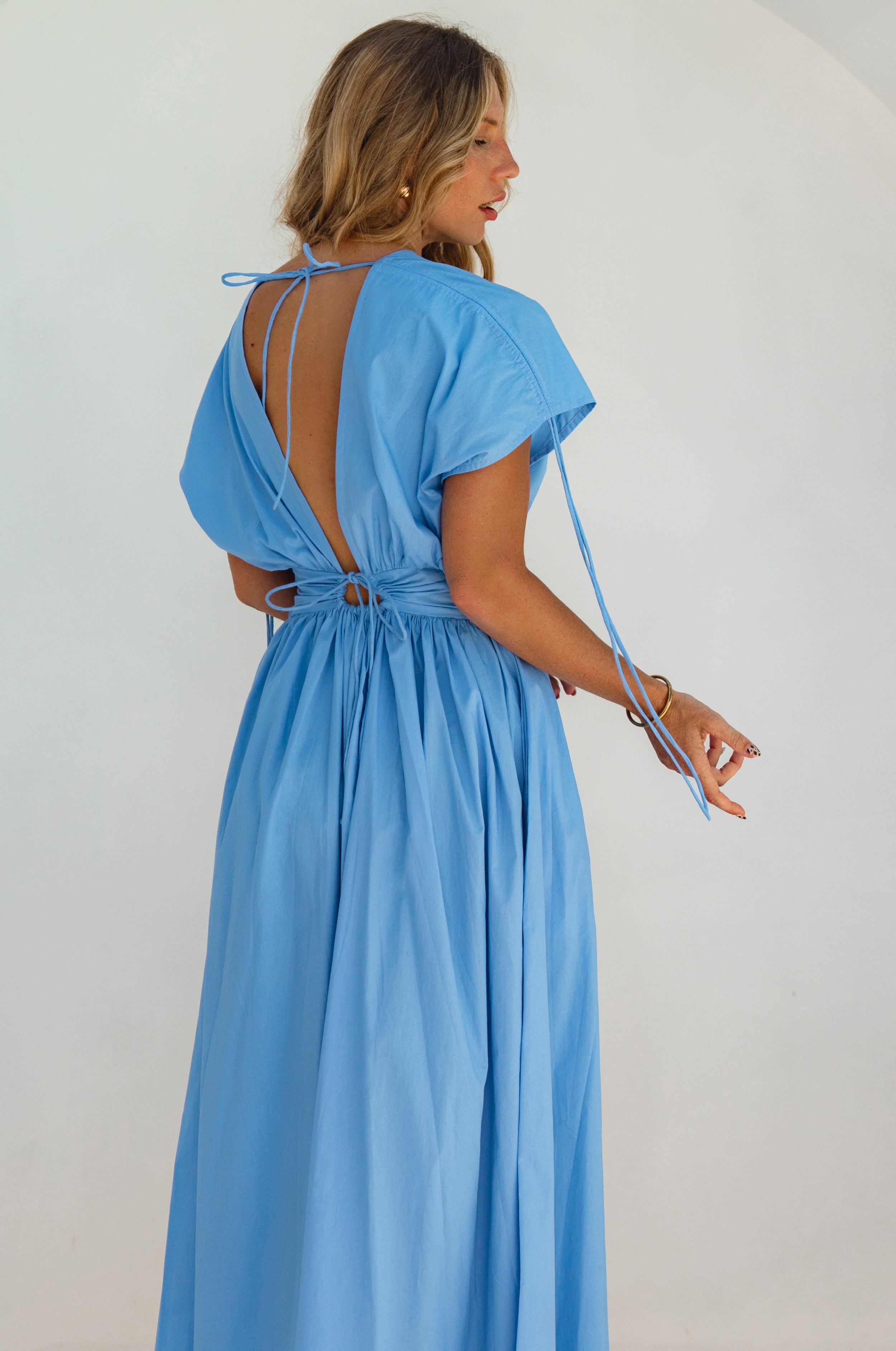 Woman wearing a blue maxi dress sleeves un-gathered and backless design on a white background