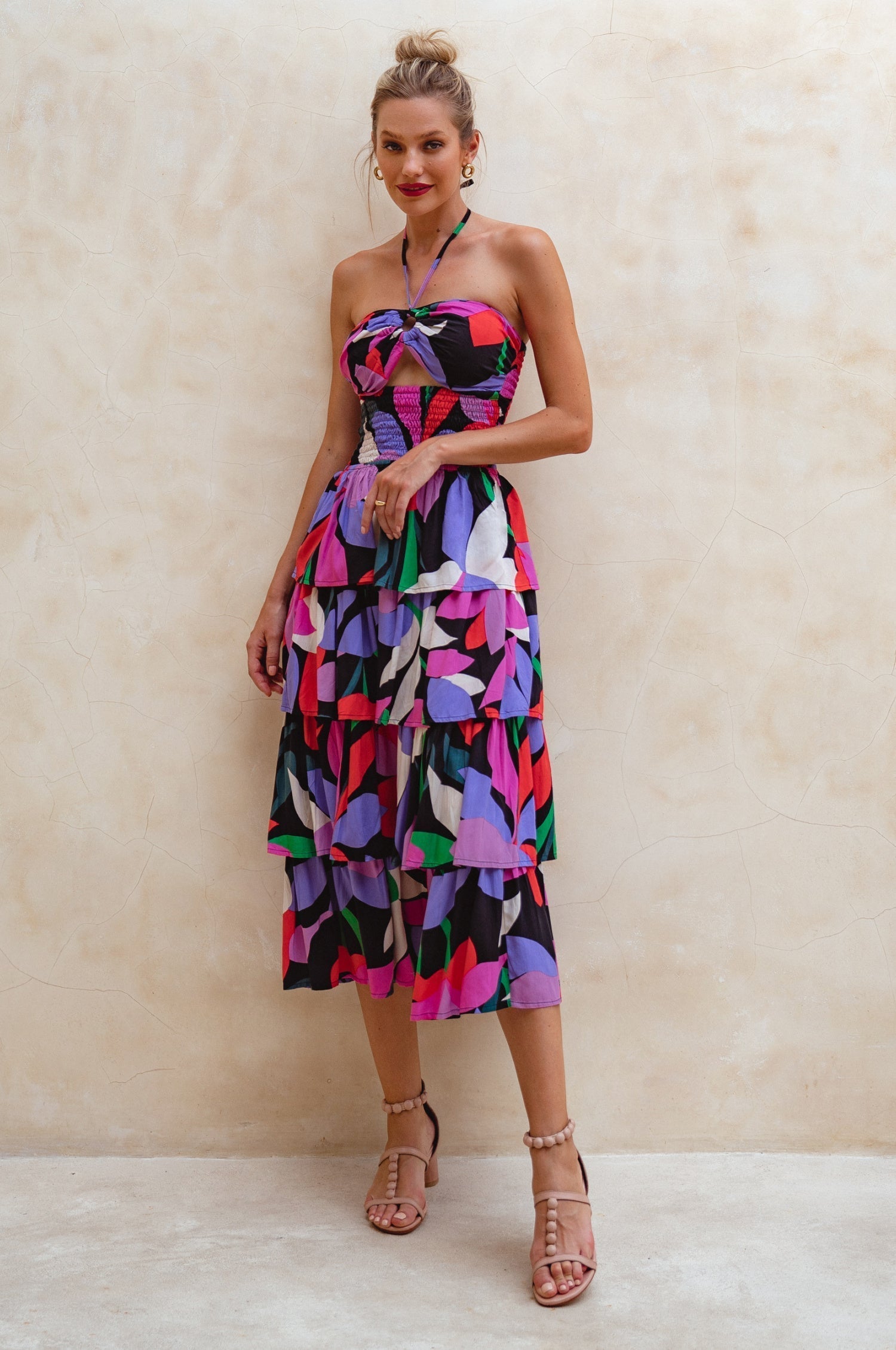 Woman wearing a colorful strapless tiered midi dress against a beige background