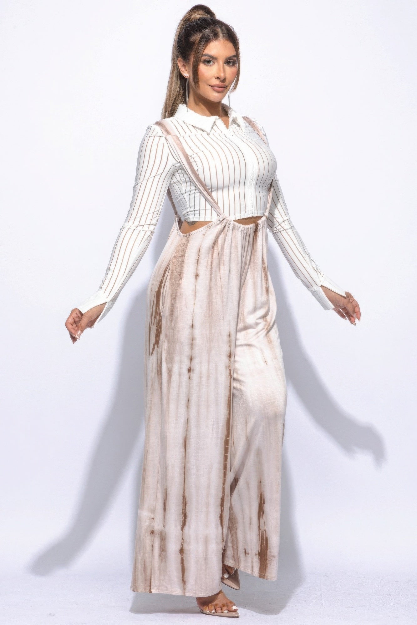 Full-length image of woman wearing Sahara Glow tie-dye jumpsuit with flowy legs and heels.