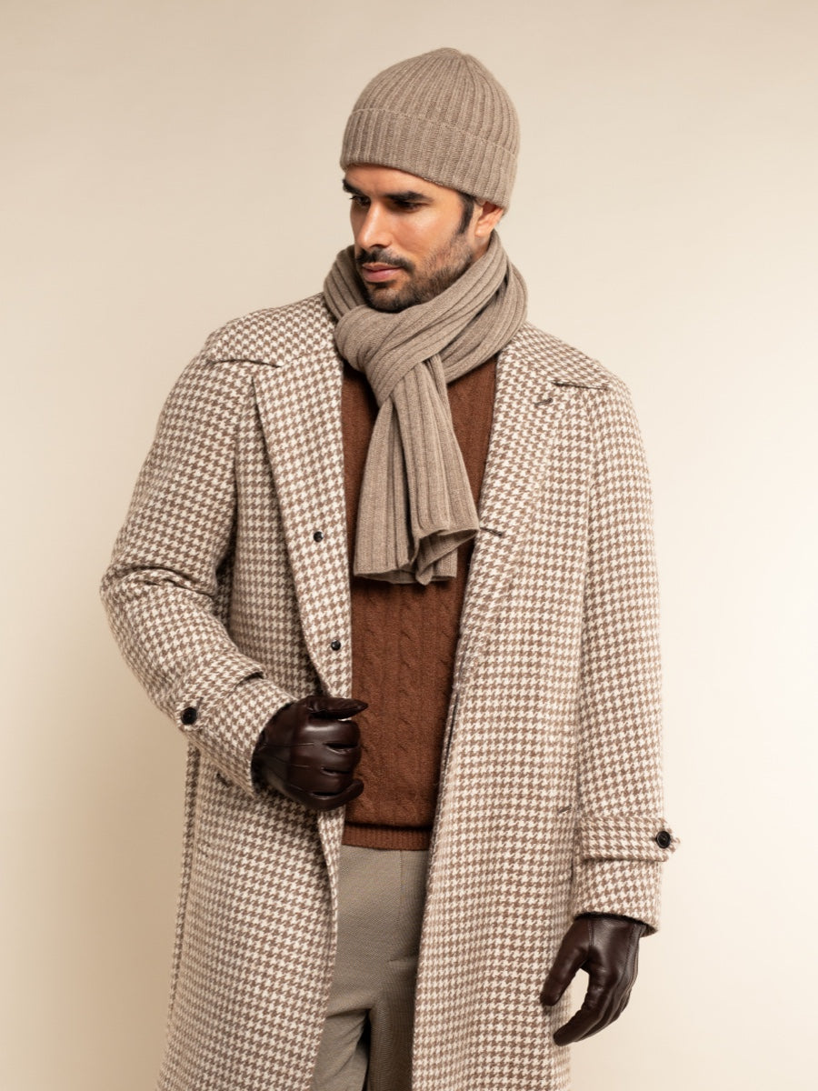 Man wearing a checkered coat, brown sweater, and brown beanie and scarf on a plain background