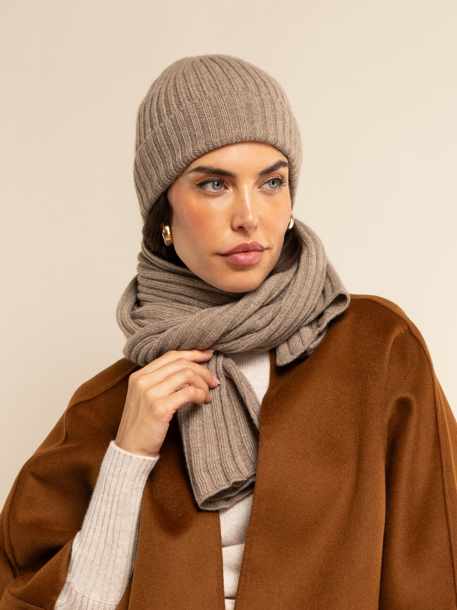 Woman wearing a brown knit hat and scarf against a beige background