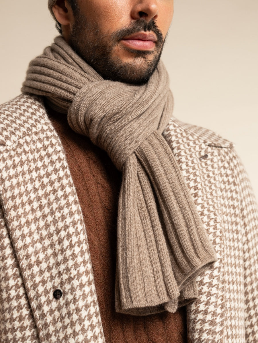 Man wearing a houndstooth patterned coat and a brown scarf against a neutral background