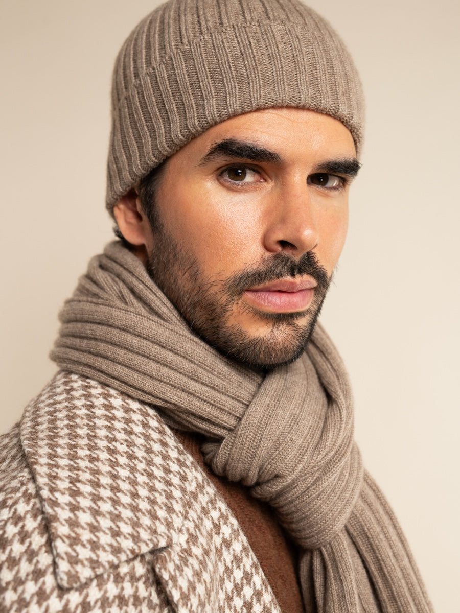 Man wearing a brown knit beanie and scarf against a beige background
