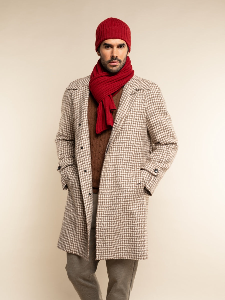 Man wearing a checkered coat, red scarf, and beanie on a beige background