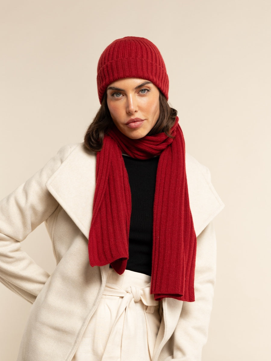 Woman wearing a red knit hat and scarf with a beige background