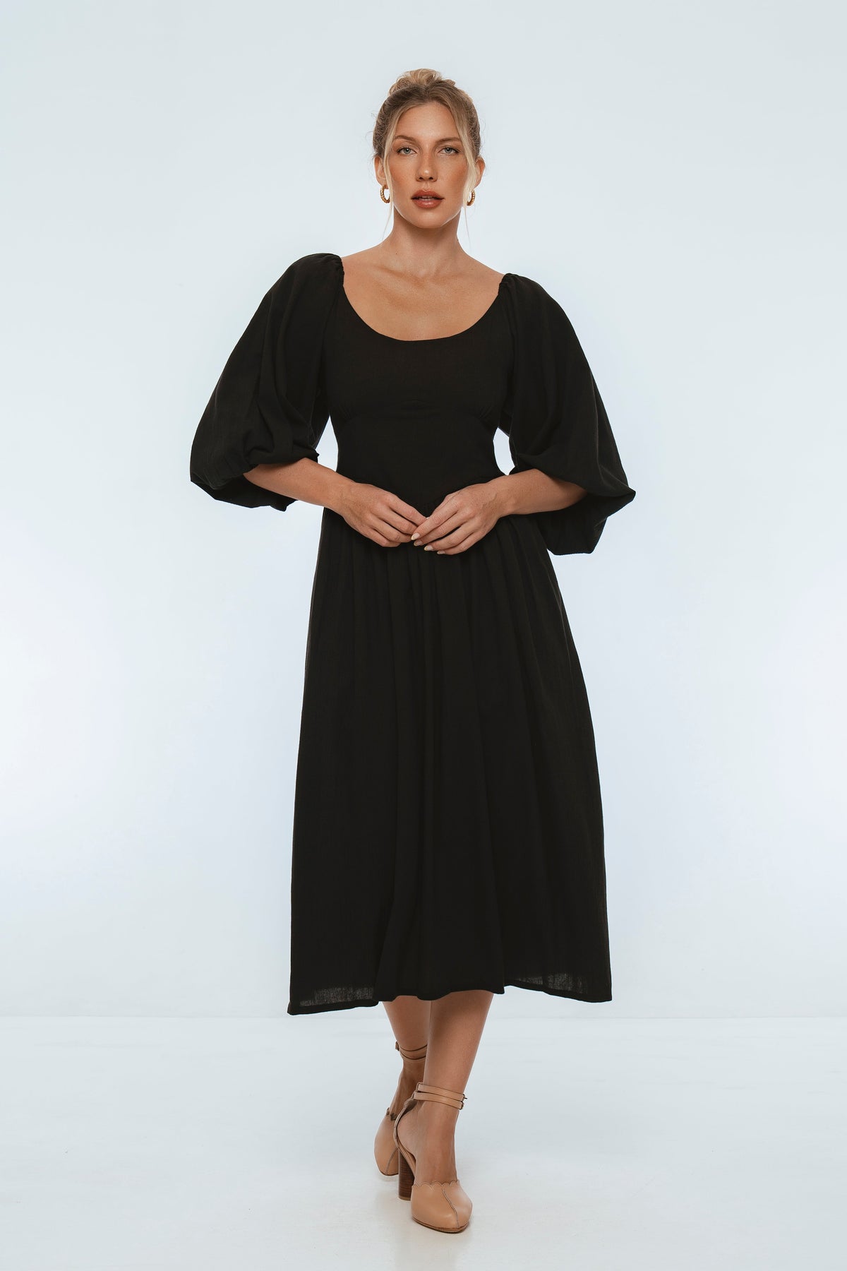 Woman wearing a black midi dress with puff sleeves and scoop neck on a white background