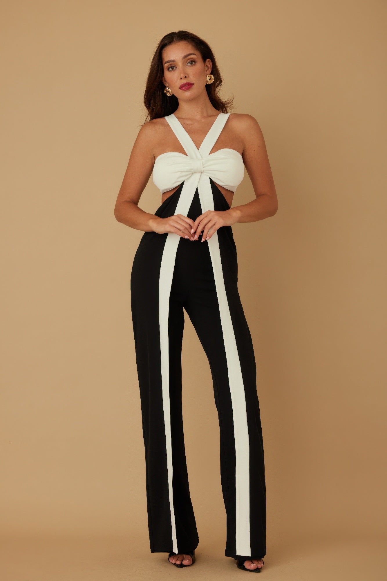 Model facing front with hands clasped, wearing black jumpsuit with white vertical stripes