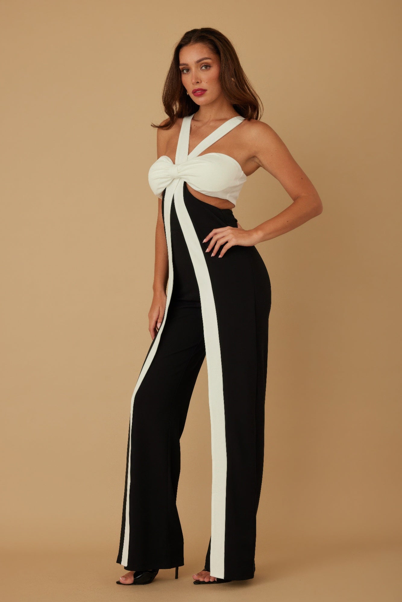 Side angle of model in halter jumpsuit showing front bow and leg panels
