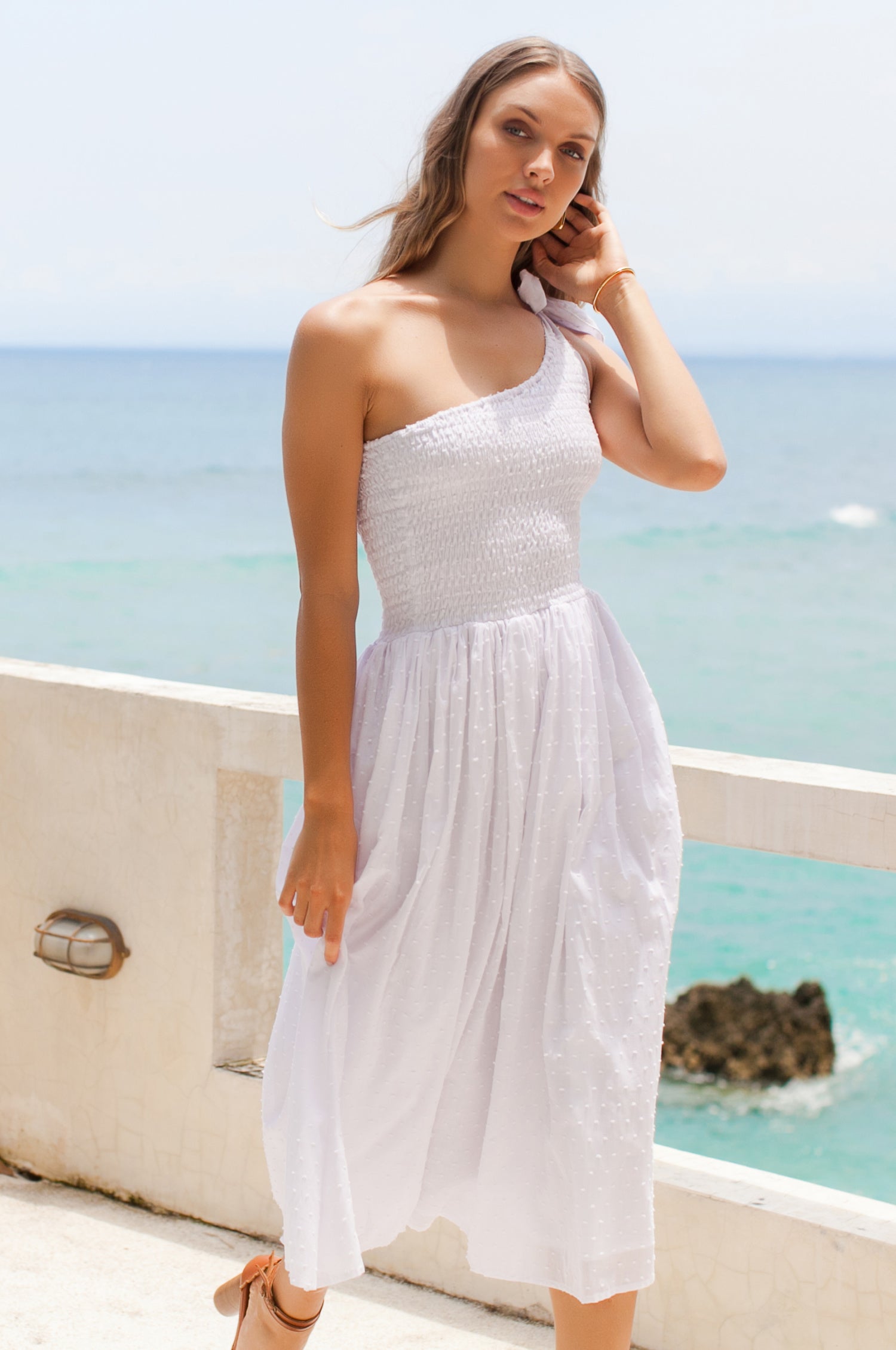 Woman wearing white one-shoulder dress with a fitted bodice, smocked at the bust, midi length, 3/4 view