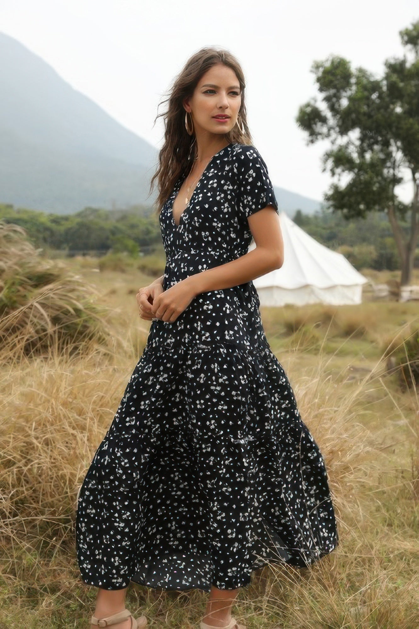 Woman in a navy floral dress standing in a field with mountains in the background