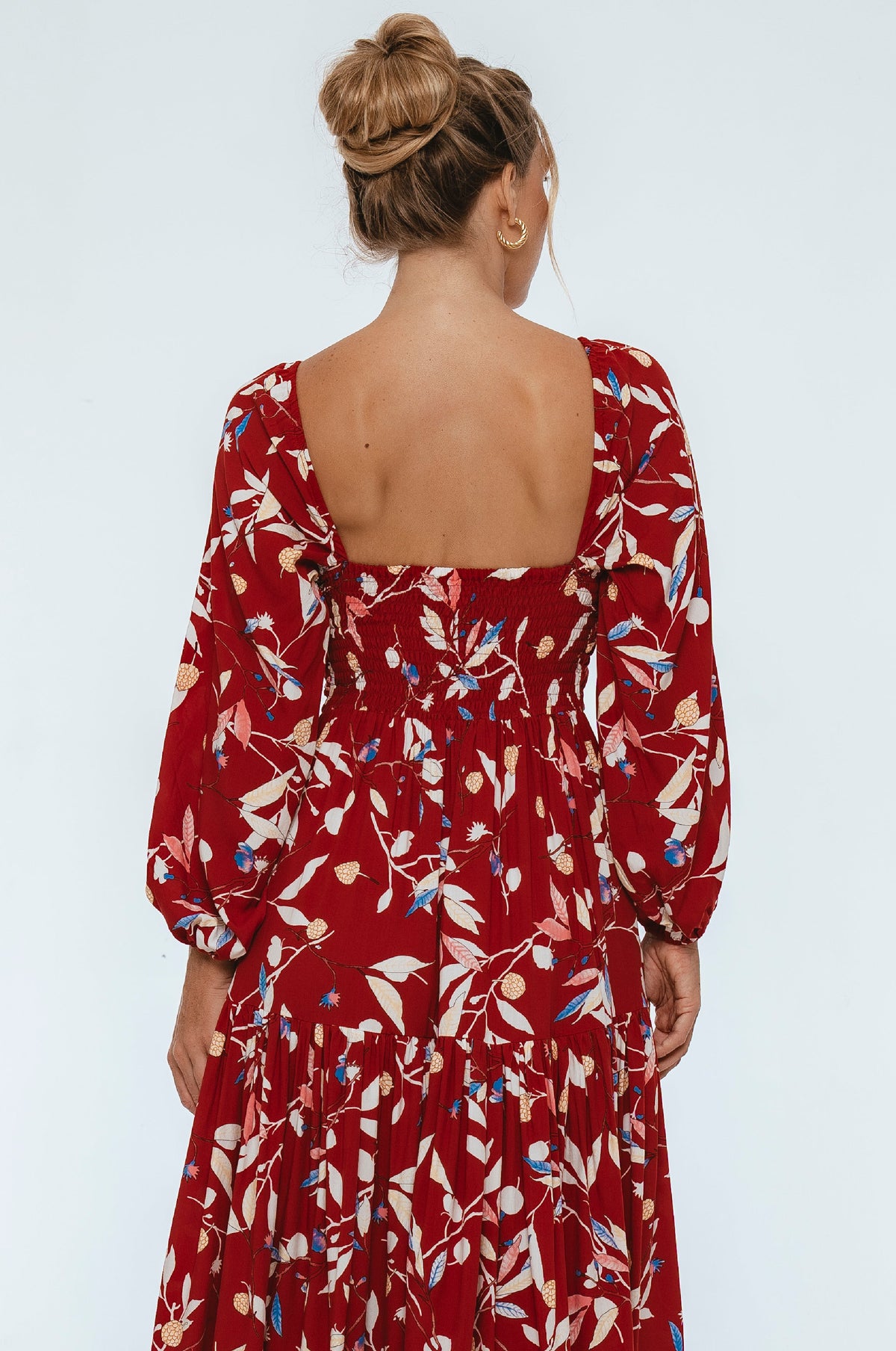 Woman wearing a red floral dress with a plain background back view