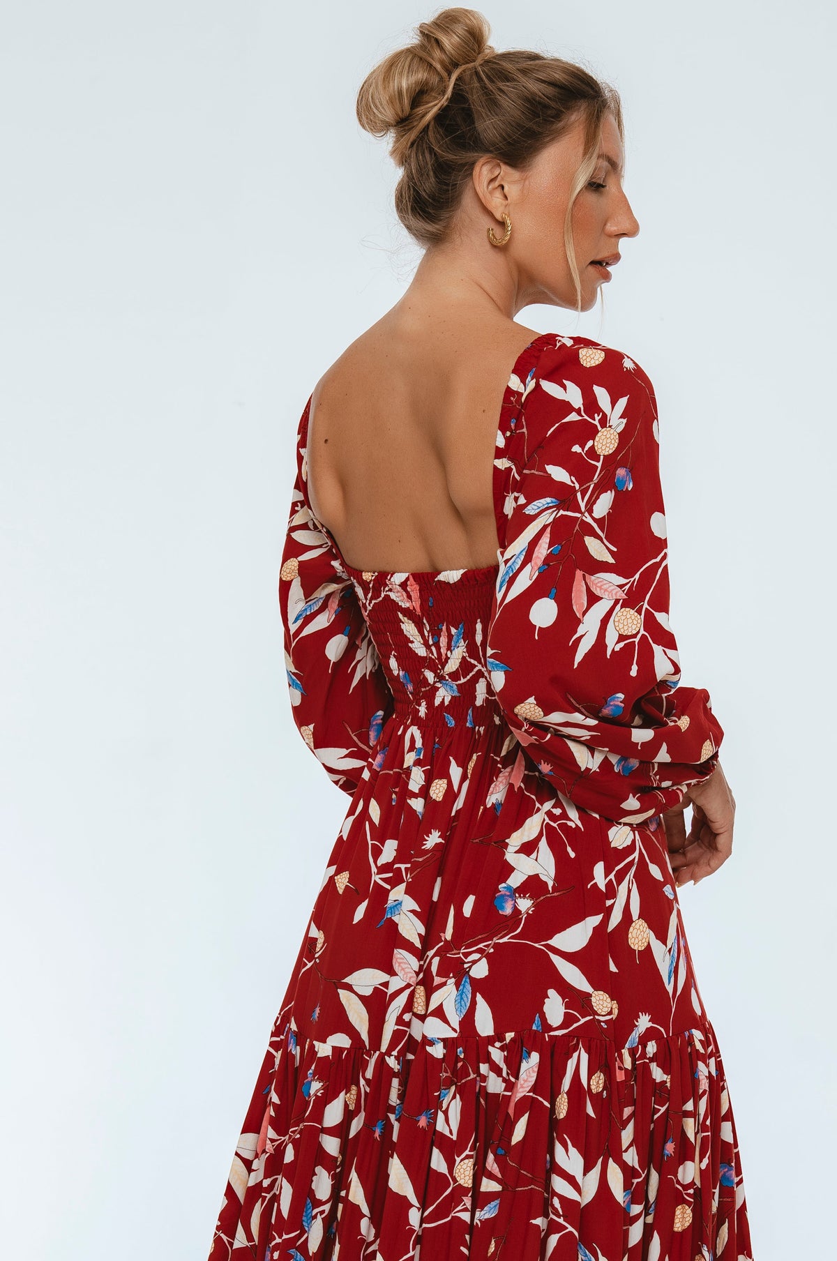 Woman wearing a red floral dress with a plain background 3/4 view