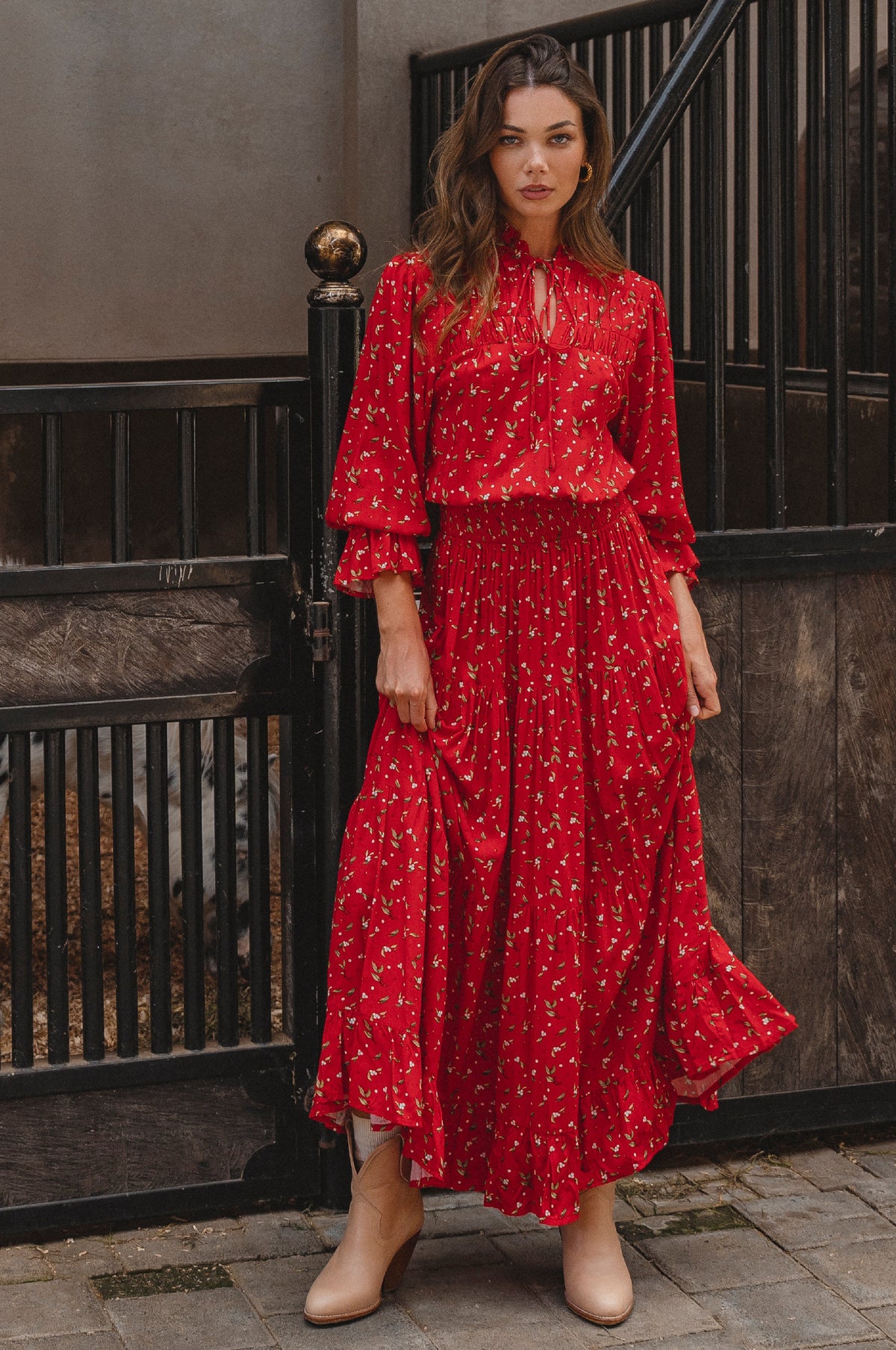 Woman wearing a red floral dress standing in front of a dark wooden door.