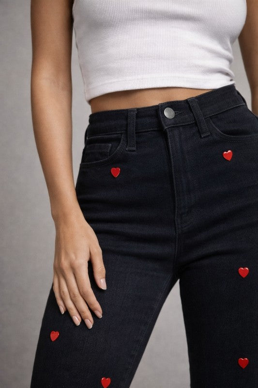 Black jeans with red heart patterns worn by model on a gray background