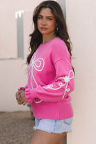 side view of pink sweater with white 3D bow detail on sleeves