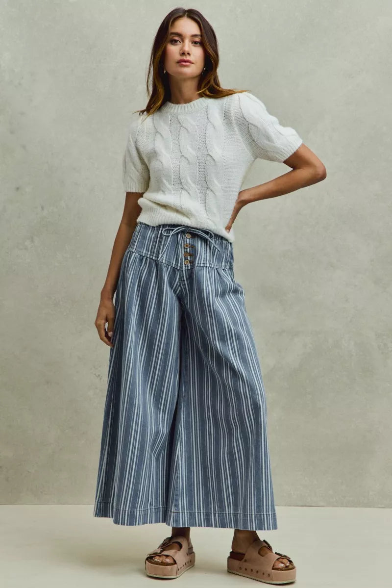 AVAH - model wearing blue and ivory striped wide leg denim pants with a white cable knit sweater and platform slide sandals.