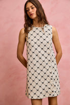 sleeveless textured mini dress featuring black bow pattern and pearl button accents front view.