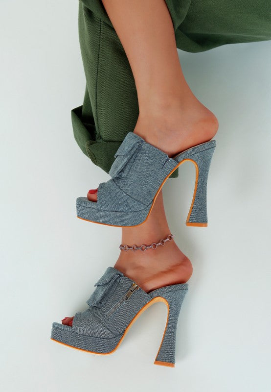Denim high-heeled shoes worn with green pants on a light background, side view