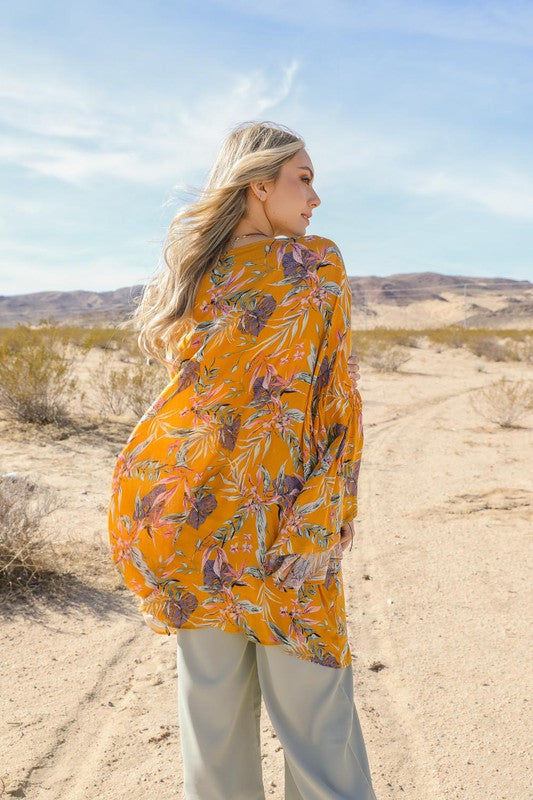 Back view of mustard yellow tropical kimono with bold floral and leaf print in the desert.