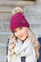 Burgundy bouclé knit hat with faux fur pom, worn with neutral scarf