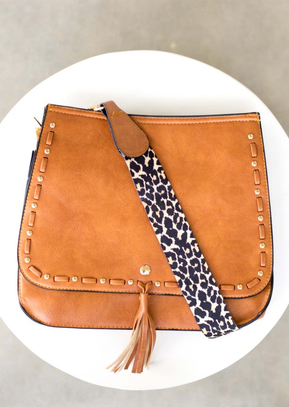 Overhead flat lay of tan fold-over bag with tassel and leopard strap
