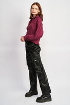 Woman wearing burgundy cable-knit collar sweater and black faux-leather pants, side angle.