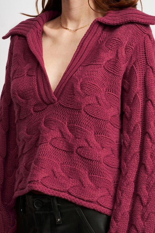 Close-up of burgundy cable-knit sweater showing deep V-neckline and textured knit.