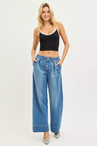 Woman wearing medium wash pleated wide leg jeans styled with a black cropped tank
