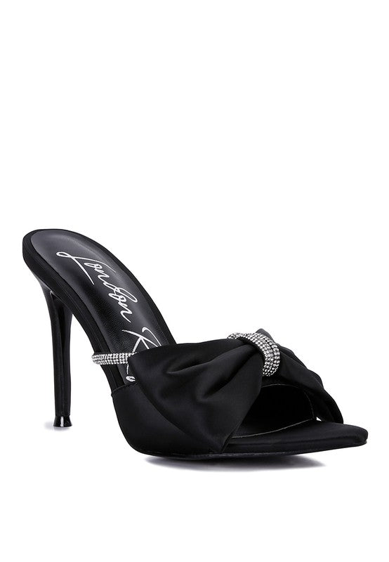 Black satin stiletto mule with rhinestone-wrapped bow detail, angled front view
