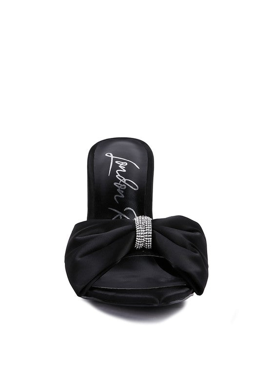Front view of black satin heel showing oversized bow and rhinestone center