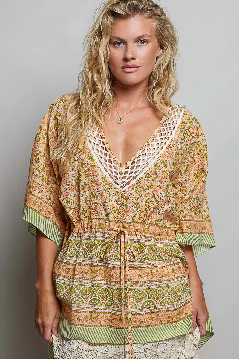 Woman wearing the Sunset Bazaar Boho Top featuring a crochet V neckline, floral print, artisan inspired border details, adjustable drawstring waist, kimono sleeves, and tassel accents.
