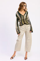 Full outfit view of olive striped cardigan styled with light pants and black heels – side angle
