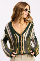 Model in olive striped cardigan looking to the side – cropped fit and front button detail visible
