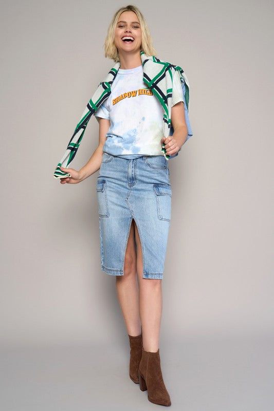 Woman wearing a patterned shirt, graphic t-shirt, denim skirt, and brown boots on a plain background