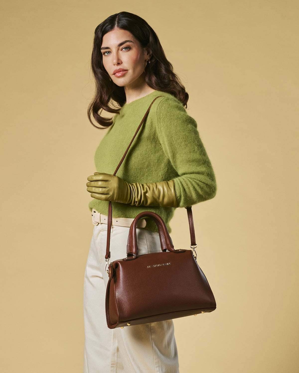 Woman holding a brown handbag against a beige background