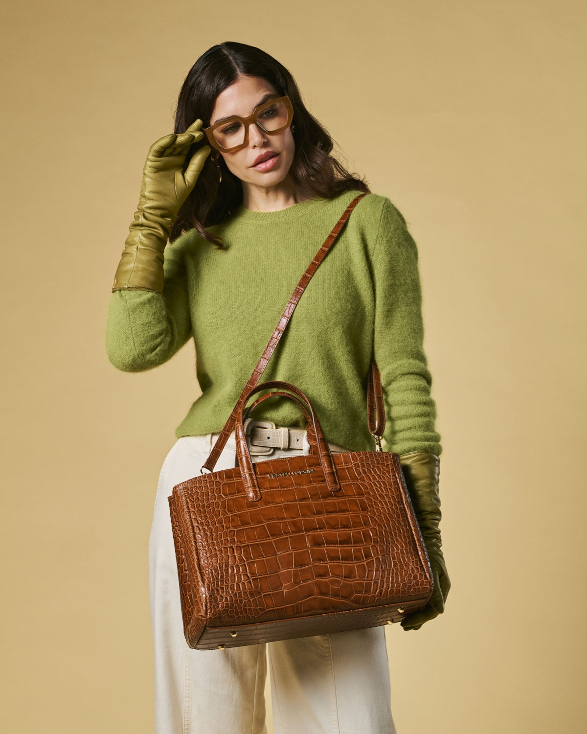 Woman holding a brown crocodile-patterned handbag against a beige background