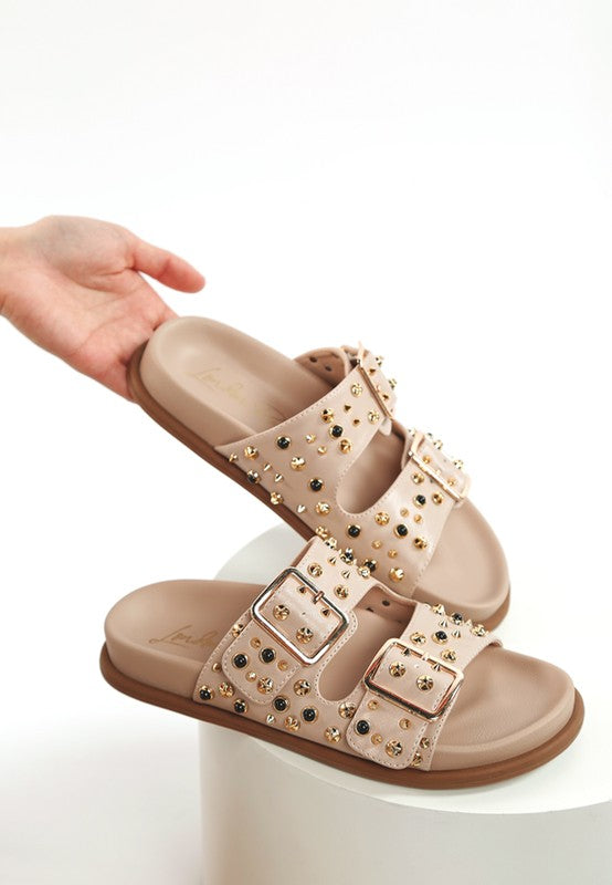 Neutral beige faux leather sandal with metallic studs and adjustable buckles displayed on white surface
