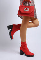 Model lifting leg to showcase red ankle boots with platform sole.
