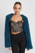 Model wearing cropped plush shrug layered over lace top and black pants, front view
