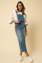 Model wearing denim overall midi dress with white tee and sneakers – front view