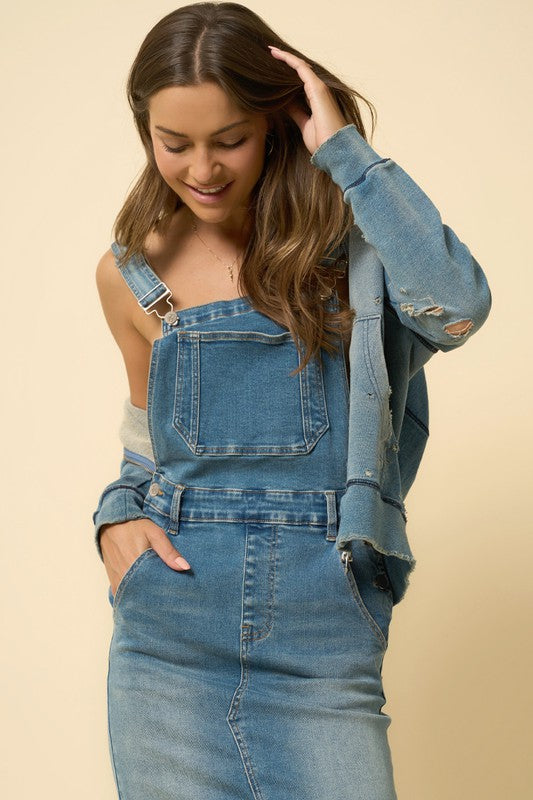 Close-up of denim bib detail with front pocket and metal buckle straps