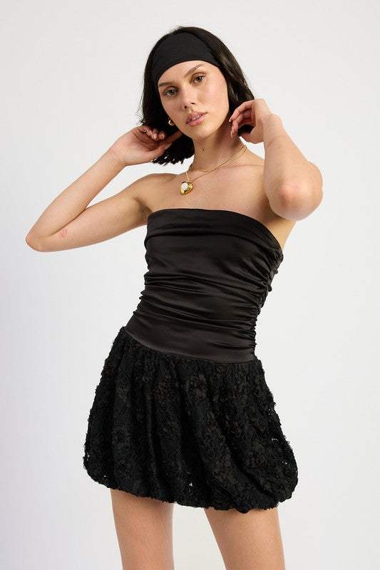A woman wearing a black strapless bubble hem mini dress with a satin bodice and lace skirt.