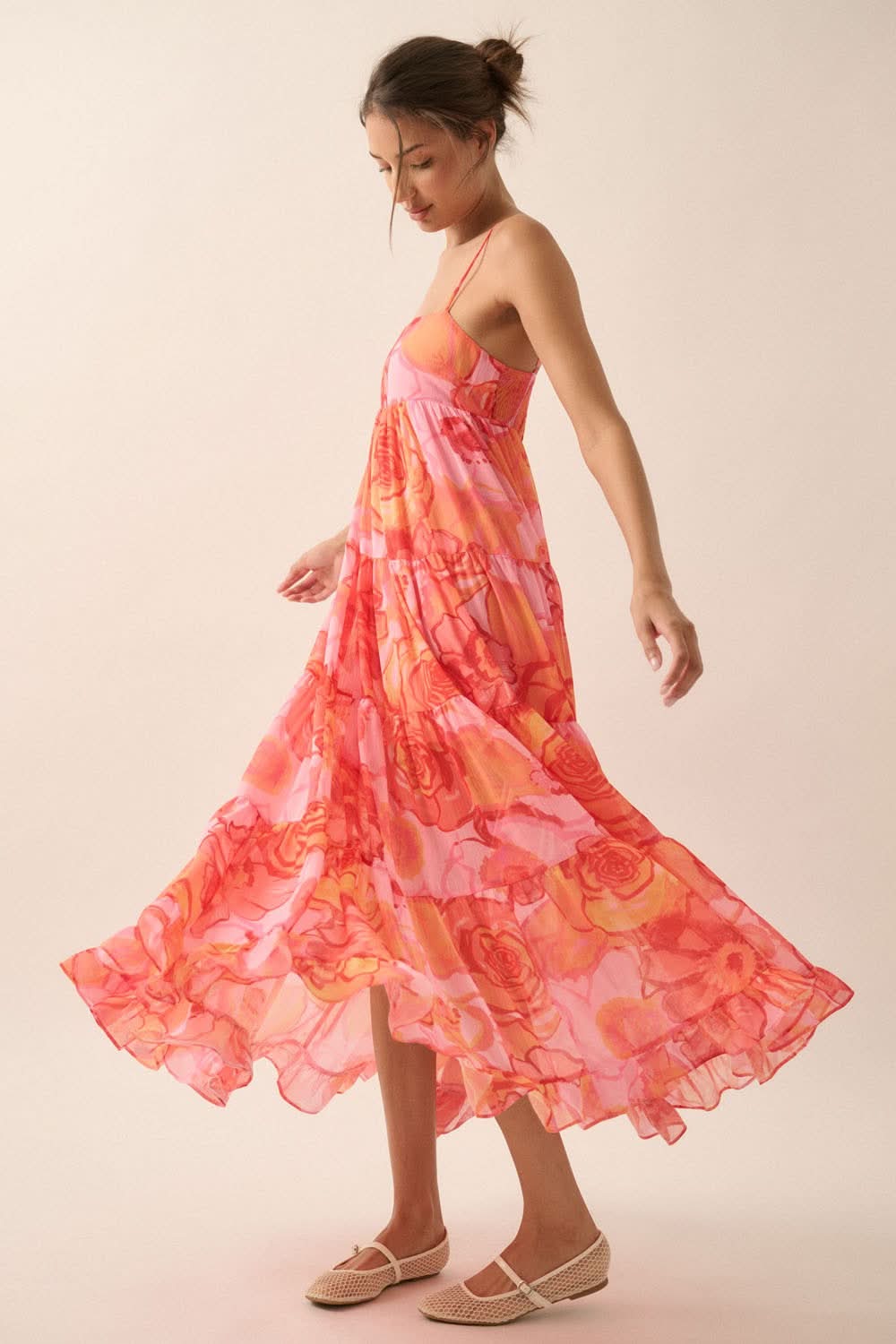 Side view of model twirling in pink floral maxi dress with flowy tiered skirt and adjustable straps, captured in motion.