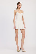 Three-quarter view of model in structured ivory pleated dress with thin straps and flared skirt