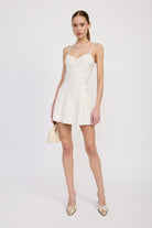 Model wearing ivory mini dress styled with heeled mules and neutral handbag