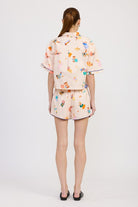 Back view of oversized cropped shirt and shorts in coordinated beach scene print, styled with minimal black flats.