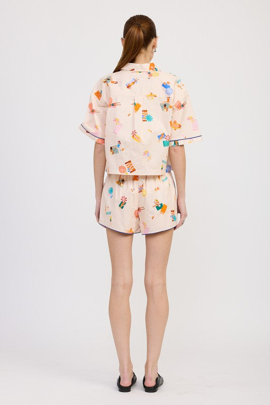 Back view of oversized cropped shirt and shorts in coordinated beach scene print, styled with minimal black flats.